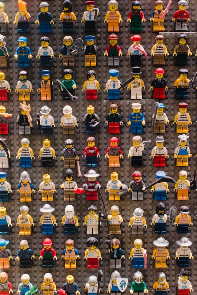 A diverse collection of Lego minifigures stand, facing the camera, on a grey Lego board.
