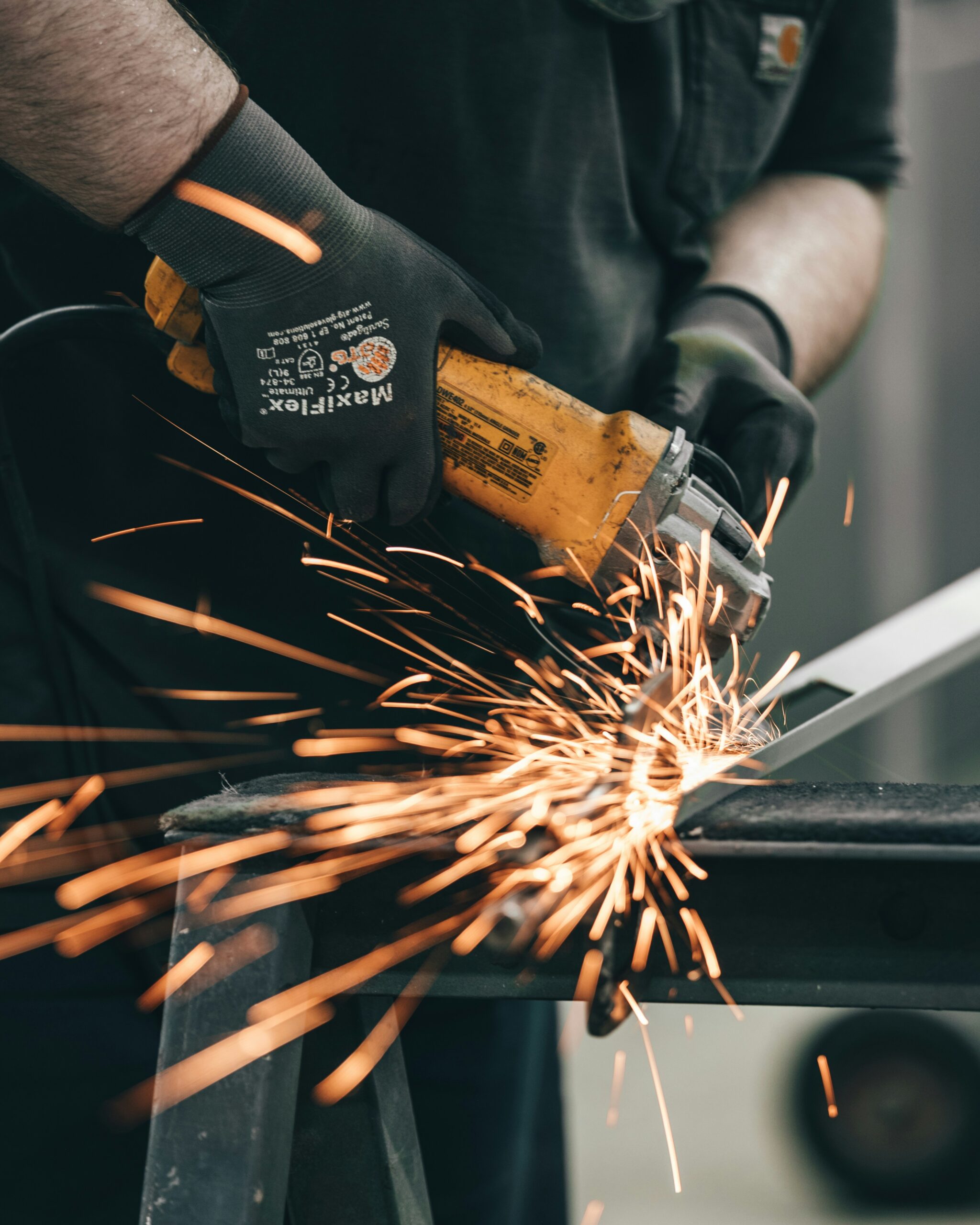 A man, wearing protective gloves, uses a grinder on a piece of metal. This creates many sparks.